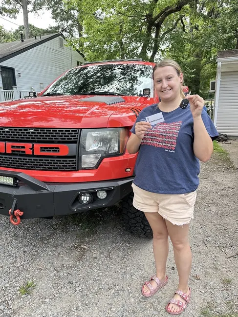 Customer receiving a replacement car key and key fob beside a red pickup truck